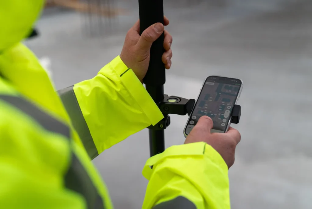 Surveyor using a GNSS receiver and mobile mapping app to collect precise location data on a construction site.