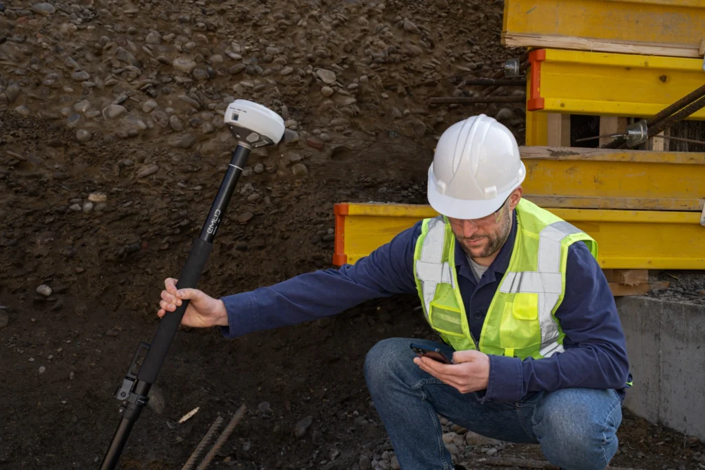Construction surveyor using a GNSS receiver and smartphone to configure field equipment at an active construction site, illustrating GNSS implementation and device migration.
